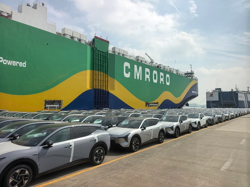Rows of silver and white XPeng L05s lined up on the quay at Nansha beside the green car carrier CM Guangzhou