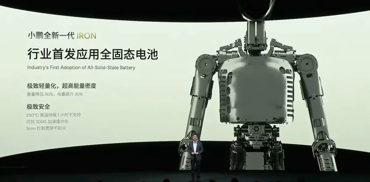 XPeng’s Tech Day slide beside a large picture of IRON’s metal frame. It reads, in Chinese and English, ‘Industry’s First Adoption of All-Solid-State Battery’, then in Chinese: extremely light with very high energy density, 30% less weight and 30% more charge; extremely safe, an hour at 250°C without losing control, a 300G impact, and no fire with a 3 mm nail driven through. He Xiaopeng stands small on the stage below.